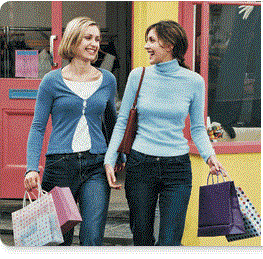 Who women holding shopping bags while walking and smiling.